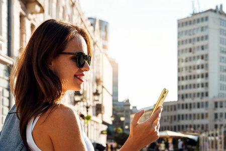 Woman wearing sunglasses checking her smartphone on city streetの写真素材