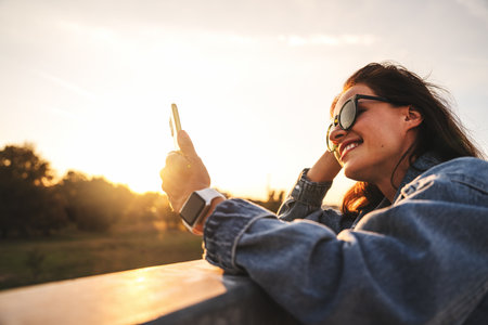 Carefree young woman using smartphone outdoors during golden hourの写真素材