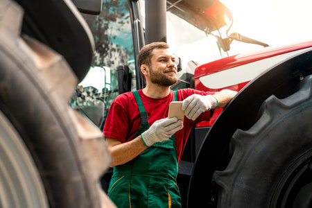 Agricultural worker standing near tractor and holding smartphone.