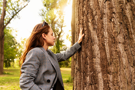Urban woman connecting with nature in city park touching tree barkの写真素材
