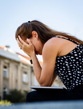 Stressed woman with head in her hands sitting outdoors in city