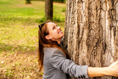 Happy urban woman hugging tree trunk outdoors connecting with natureの写真素材