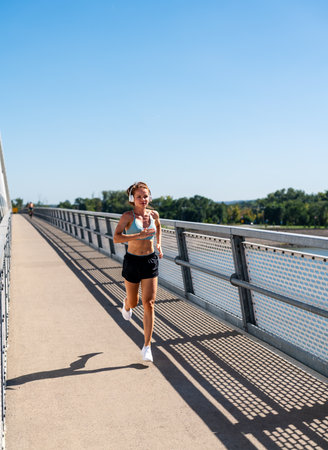 Fitness woman runs on pedestrian bridge in the city in summer.の写真素材