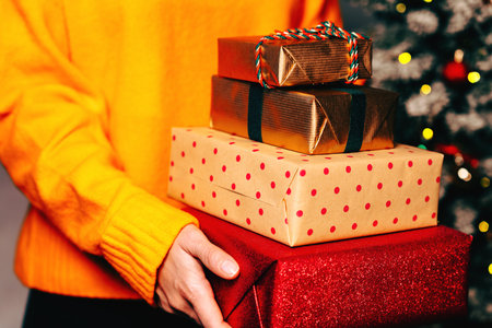 Stack of Christmas gift boxes in the hands of woman wearing warm yellow sweater.