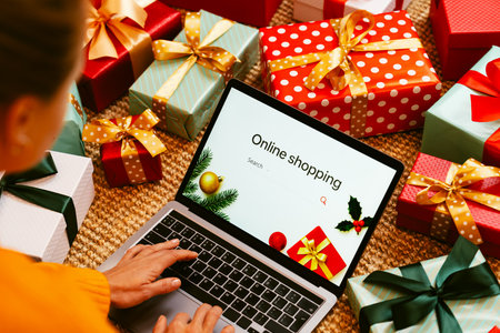Woman using laptop with sign on screen Online Shopping and Christmas gifts on the floor.の写真素材