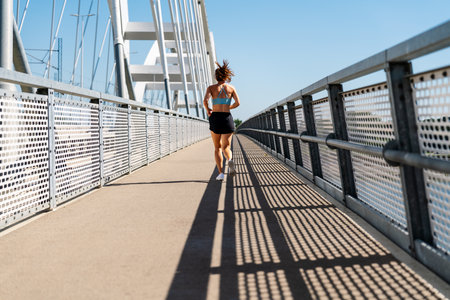 Back view of a female athlete running on the city bridge in summer.の写真素材