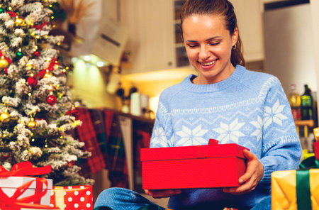 Smiling woman holding Christmas presents in cozy home atmosphereの写真素材