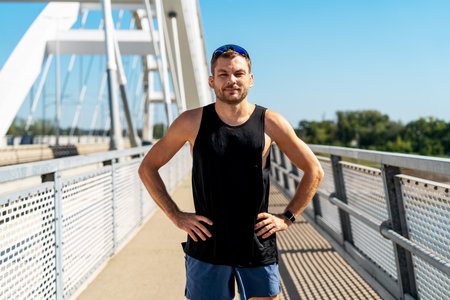 Portrait of male jogger wearing sportswear posing on urban bridge in summer.