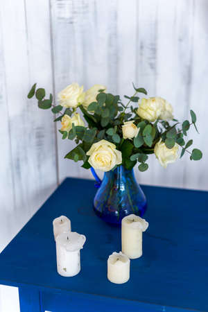 white flowers, roses in a blue vase on a blue table with a white wooden background.の写真素材