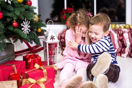 Two small children, brother and sister, are sitting on the background of the Christmas interior and...