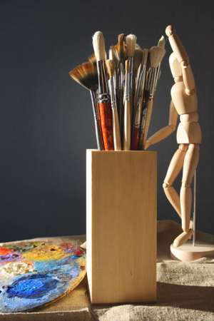 Art brushes in a wooden glass with a palette and model on a dark background.の写真素材