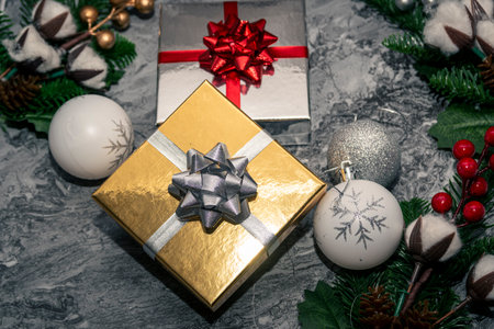 Gold and silver wrapped gift boxes surrounded by baubles, berries and evergreen branches, traditional Christmas flatlay on stone background.の写真素材