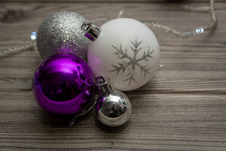 Purple, white and silver Christmas baubles on wooden table with soft fairy lights, cozy holiday decoration still life.の写真素材