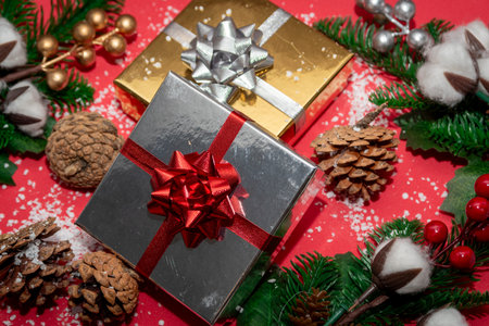 Silver gift box with red bow and golden box with silver bow among pine cones and greenery on red...