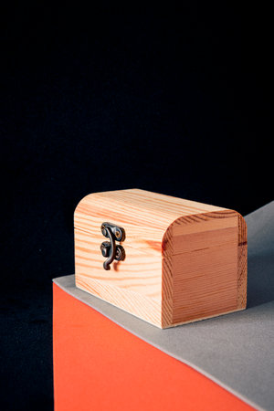 Small wooden chest with metal clasp on orange and gray geometric surface against dark background, modern still life product mockup with copy space.の写真素材