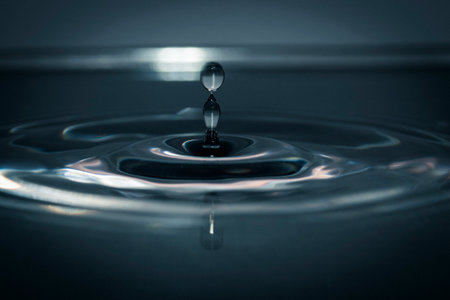 Artistic macro of a tall water column with droplet and reflection, frozen in time with smooth...
