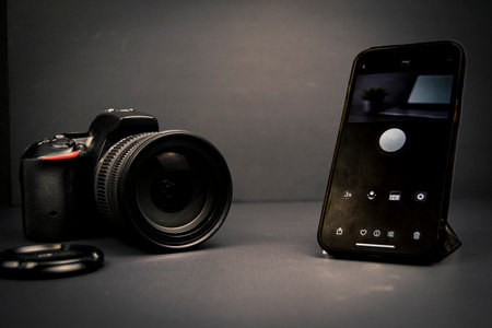 DSLR camera next to a smartphone showing a camera app interface on a dark background. Concept of mobile photography and creator workflow.の写真素材