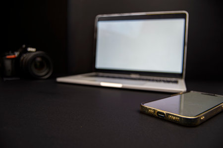 Low-key workspace with laptop mockup, DSLR camera and smartphone on black background. Ideal for tech, photography, remote work and copy space.の写真素材