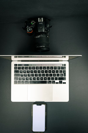 Top-down flat lay of laptop keyboard with DSLR camera and smartphone blank screen on dark background. Minimal tech workspace mockup with copy space.の写真素材