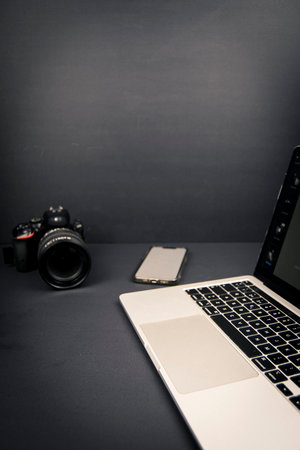 Dark minimalist desk scene with camera, laptop edge and blank smartphone screen, plenty of negative space for text and design layouts.の写真素材