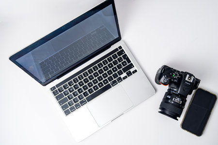 Top view flat lay with laptop, DSLR camera and smartphone on white background. Clean minimal mockup...