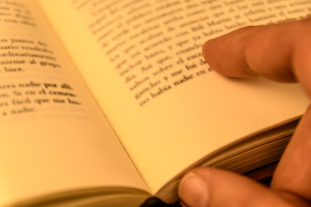 Close-up of a hand turning a book page with warm light and shallow depth of field. Concept of...
