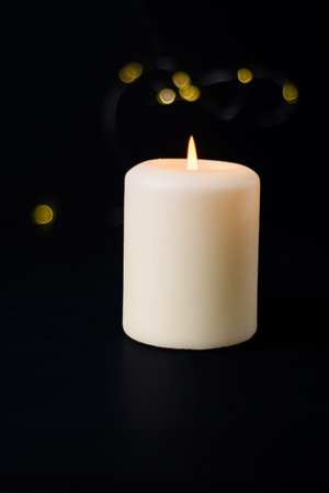 Small lit candle with soft bokeh on dark background and generous copy space for text.の写真素材