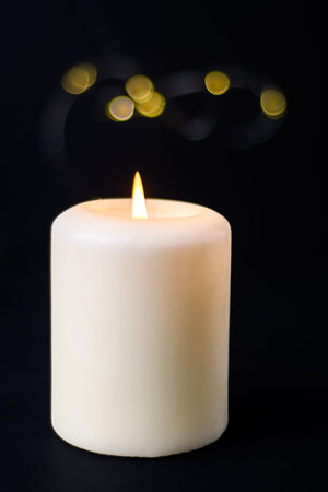 Lit white candle with warm bokeh lights on dark background, cozy relaxation and wellness mood.の写真素材