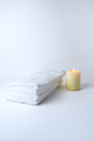 Minimal spa still life: folded white towels and a small burning candle on a soft light background with copy space.の写真素材