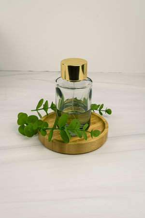 Minimal wellness still life: clear glass fragrance bottle with gold cap on bamboo tray and...