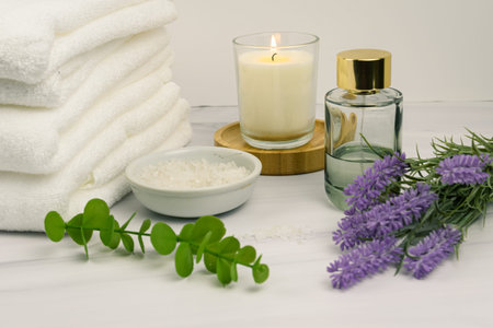 Wellness home spa still life: folded white towels, lit candle, bath salts, lavender and eucalyptus...