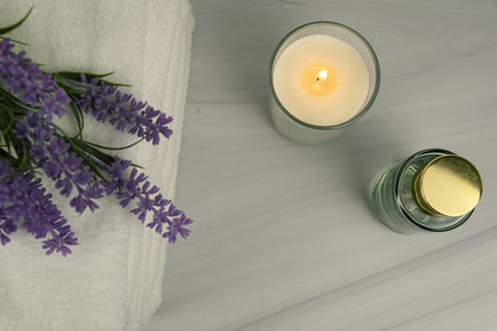 Top view flat lay with lit candle, perfume bottle and lavender on a marble surface. Minimal wellness spa concept with copy space.の写真素材