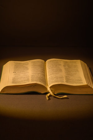 Open Bible on a dark table under warm light, with a black background and copy space. Christian...