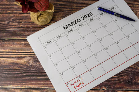 Flat lay of March 2026 calendar with Holy Week noted, blue pen and floral decoration on rustic wood, concept of Easter planning and religious tradition.の写真素材