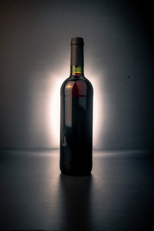 Backlit wine bottle on a dark background with a glowing halo and subtle red tones visible in the glass, a dramatic minimalist image for luxury wine, branding and editorial use.の写真素材