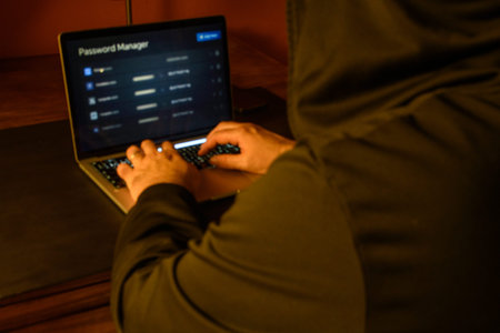 Hooded person using a laptop with password manager on screen, conceptual image of credential...