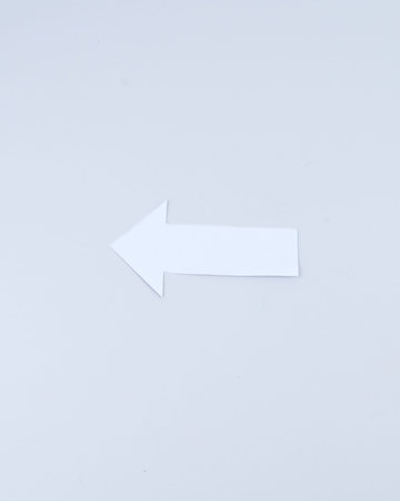 Single white paper arrow pointing left on a clean background, minimalist concept for direction, return, navigation, choice and decision making.の写真素材