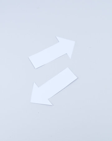 Two diagonal white paper arrows pointing in opposite directions on a minimal background, conceptual...