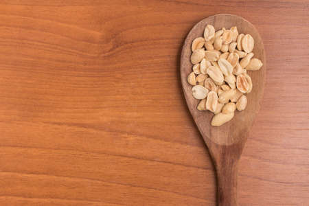 Peanuts into a spoon over a wooden tableの写真素材