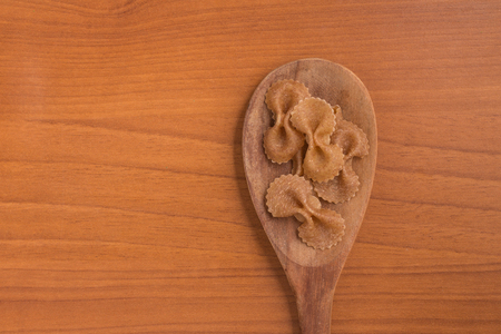 Wholegrain Farfalle into a spoon. wholemeal. Integral over a wooden tableの写真素材