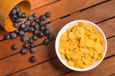 Corn Flakes and blue barry into a bowl over a wooden table