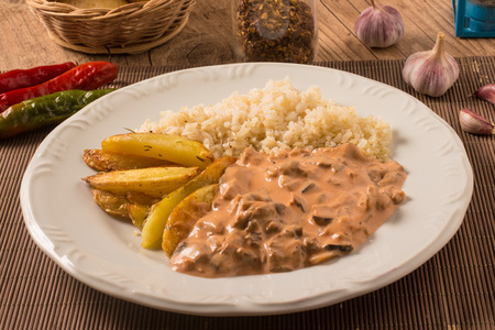 Vegetarian Mushroom Stroganoff with rice and rustic potatoes over a wooden tableの写真素材
