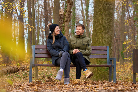 Man and woman sitting on bench in autumn park and talkingの写真素材