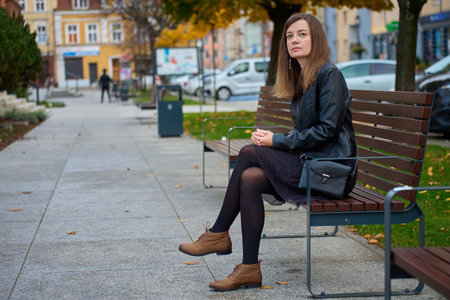 Woman in black jacket sitting on city benchの写真素材