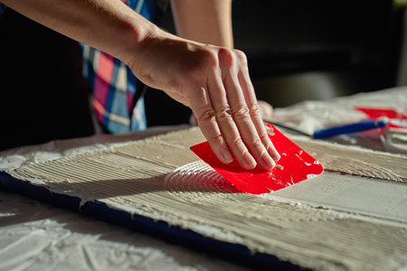 Hand pressing red plastic scraper into thick paste to create circular textured linesの写真素材