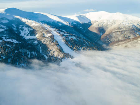 Aerial shot of majestic sunrise in the mountains. Valley between the mountains is covered with fog and is illuminated by the warm rays of the rising sun. Mountains covered with forest natural.の写真素材