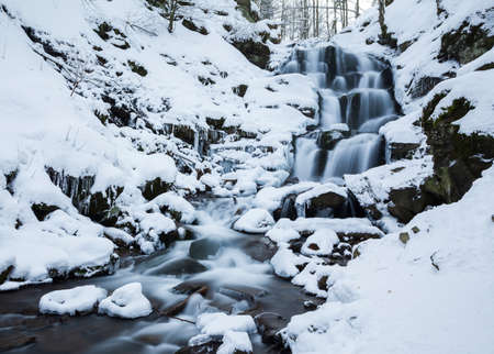 Winter mountain waterfall snow scene. Snowy mountain waterfall landscape. Winter mountain waterfall in Shipot waterfall - Carpathian Mountains, Ukraine.の写真素材