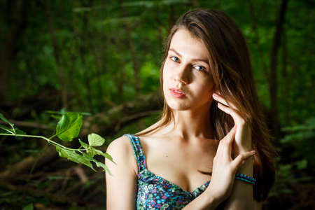 Beautiful young woman wearing elegant white dress walking on a forest path with rays of sunlight beaming through the leaves of the treesの写真素材