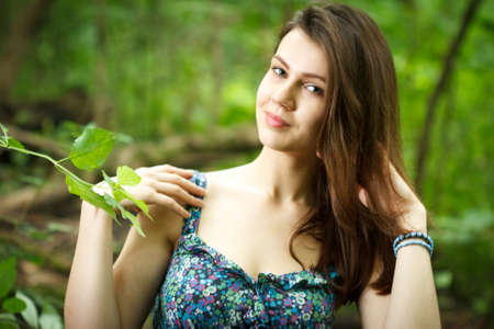 Beautiful young woman wearing elegant white dress walking on a forest path with rays of sunlight beaming through the leaves of the treesの写真素材