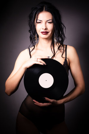 Vintage photo of a glamorous pinup girl, holding a vinyl record and looking up on a pink background.の写真素材